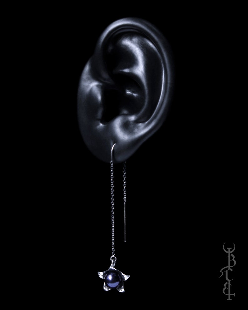 May include: A silver dangle earring with a black pearl and a star-shaped design. The earring is hanging from a black chain.