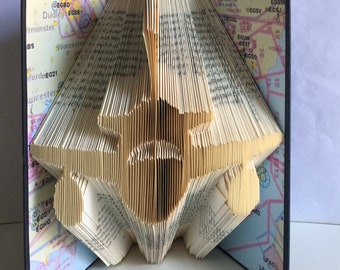 May include: A book folded into the shape of an airplane. The book is open and the pages are folded to create the shape of the airplane. The book is on a white surface.