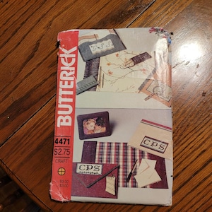 May include: A vintage Butterick craft pattern envelope, featuring various craft projects. The envelope is red with the Butterick logo and product details. The projects include framed photos, embroidered designs, and stationery.