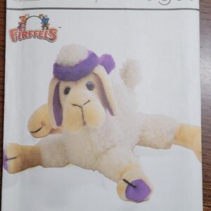 May include: A Simplicity crafts pattern for a Firefells stuffed sheep and camel toy. The pattern features a plush sheep with a purple hat and accents. The pattern's title is "Shamel Sheep and Camel".