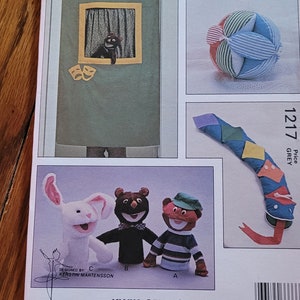 May include: A sewing pattern for making puppets and a stuffed ball. The pattern is called "Kwik-Sew" and the number is 1217. The pattern includes instructions for making a bunny, a bear, and a boy puppet. The stuffed ball is made of fabric with stripes and different colors.