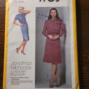 May include: Simplicity sewing pattern number 9705 for a dress. The pattern is for a miss or jeune femme. The pattern includes two dress styles. The first style is a blue dress with a collar and short sleeves. The second style is a pink dress with a collar, long sleeves, and a belt. The pattern is designed by Jonathan Hitchcock for Reuben Thomas.