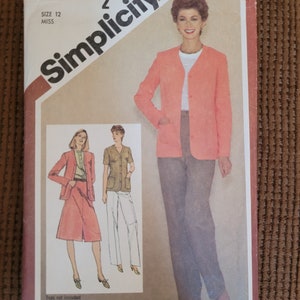 May include: Simplicity sewing pattern number 9870 size 12 miss. The pattern includes instructions for a jacket and pants. The jacket is a light pink color and the pants are a brown color. The model is wearing the jacket and pants. The pattern is on a white background.