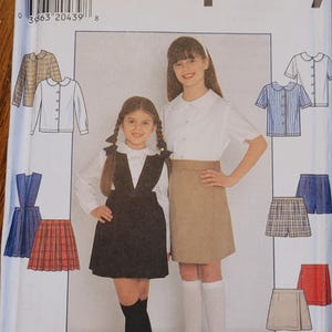 May include: Simplicity sewing pattern envelope featuring school uniform designs for girls. The envelope shows illustrations of various outfits, including jumpers, skirts, and blouses. The size range is indicated on the top left corner of the envelope.