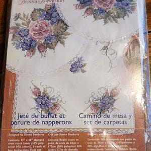 May include: A Bucilla Bee's Delight dresser scarf and doily set kit designed by Donna Dewberry. The package includes stamped cross stitch fabric, 6 yards of lace, and instructions. The dresser scarf measures 15 inches by 68 inches.