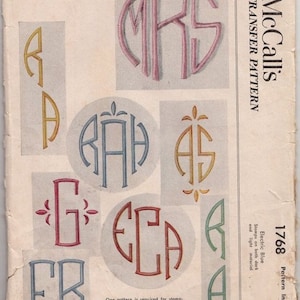 May include: A vintage McCall's transfer pattern for monogramming. The pattern includes a variety of initials in different styles and colors, including "MRS", "RAH", "AS", "G", "ECA", and "ER". The pattern is for electric blue fabric and includes instructions for stamping a single initial, two-letter monogram, or three-letter monogram.