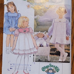 May include: Vintage Butterick sewing pattern for Cabbage Patch Kids outfits. The pattern features illustrations of children in dresses, with the Cabbage Patch Kids logo and text. Includes iron-on transfers.