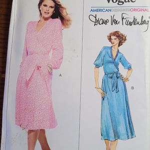 May include: Vogue sewing pattern featuring two wrap dresses. The pattern includes a pink, long-sleeved dress with a belt and a blue, short-sleeved dress with a tie. The pattern is designed by Diane Von Furstenberg.