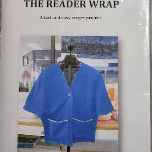 May include: A white paper pattern with the text "THE READER WRAP" and "A fast and easy serger project."  The pattern features a photo of a blue cardigan with a button closure and two pockets. The text "Rally Style" is at the bottom of the pattern.