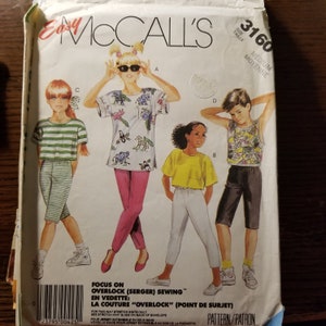 May include: A sewing pattern for children's clothing. The pattern includes four different designs: a green and white striped shirt, a pink and white shirt with a colorful animal print, a yellow shirt, and a black and white tank top. The pattern is for size medium and is called "Easy McCall's 3160".