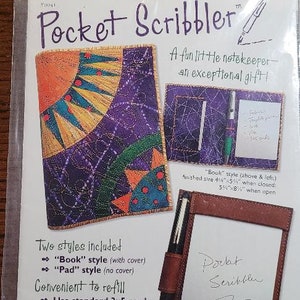 May include: A package for a Pocket Scribbler notekeeping kit. The kit includes two styles: a "Book" style with a cover and a "Pad" style without a cover. The package shows a purple and yellow fabric "Book" style and a brown leather "Pad" style. The package also includes instructions for embellishing the cover and a bonus gift tag.