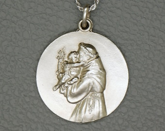 May include: Silver pendant necklace featuring a detailed relief of Saint Anthony of Padua holding the Christ Child. The pendant is round and has a smooth, polished finish.