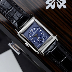 May include: A rectangular silver-tone watch with a textured blue dial, silver hands, and indices. The dial features a sub-dial with the text DAY and NIGHT, and the brand name Jaeger-LeCoultre. It has a black alligator-patterned leather strap.