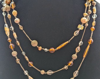May include: A multi-strand necklace with gold chain and amber colored beads. The necklace features a variety of bead shapes and sizes, including round, oval, and faceted.