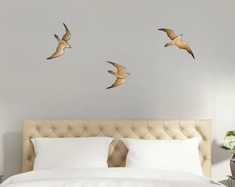 May include: Three gold-colored bird wall decals on a light gray wall above a beige headboard with white bedding.