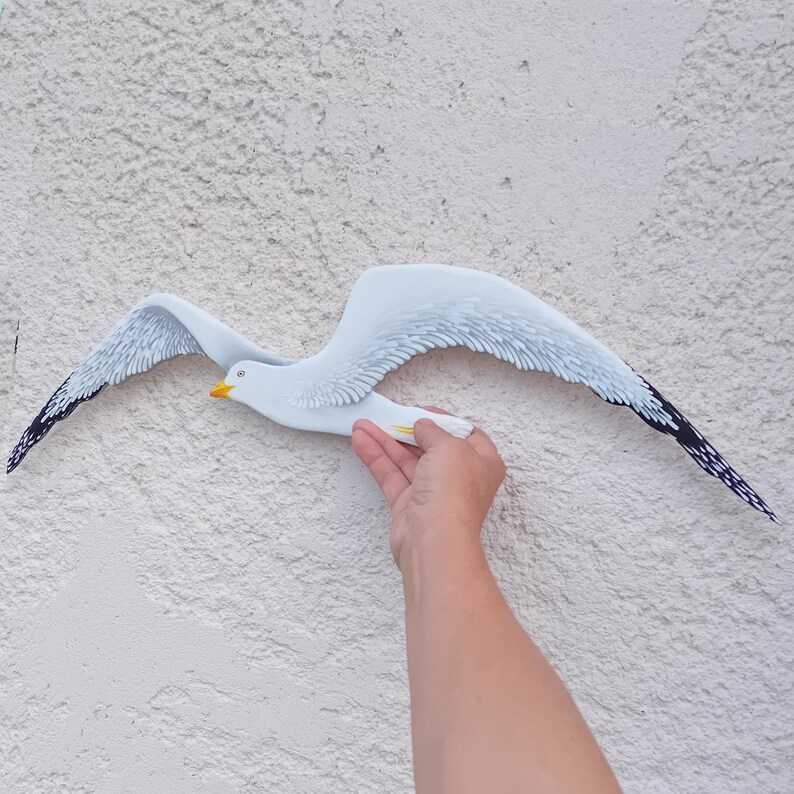 and holding a hand-painted wooden seagull – handmade coastal wall decor