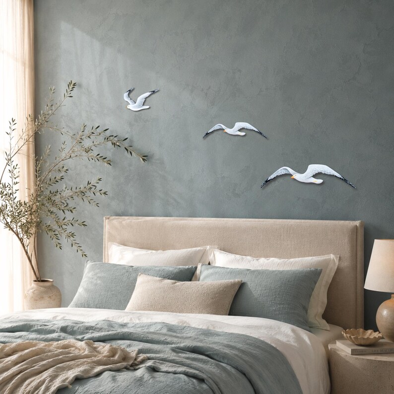 Set of three white wooden seagulls displayed above a bed – coastal bedroom wall decor idea.