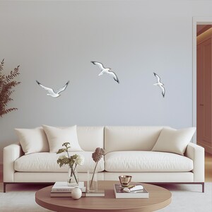 Coastal wall art installation with flock of 3 flying seagulls above sofa in living room