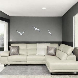 Coastal wall art installation with flock of 3 flying seagulls above white sofa
