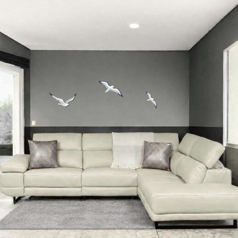 Coastal wall art installation with flock of 3 flying seagulls above white sofa