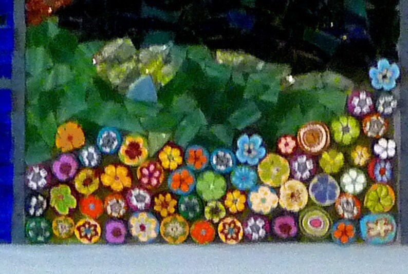 May include: A close-up of a mosaic art piece featuring a row of colorful, crocheted flowers. The flowers are arranged in a semi-circle and are made of various colors, including red, orange, yellow, green, blue, and purple.