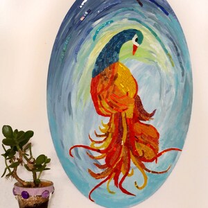 May include: A mosaic artwork depicting a colorful bird with a long, flowing tail. The bird is made of small, colorful tiles and is set against a blue and green background.
