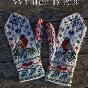 以下が含まれることがあります： 赤いコマドリと緑色の松の木の模様がついた白いニットの手袋のペア。手袋は赤、白、緑の縁取りがされています。画像の上部に「Winter birds」というテキストがあります。画像の下部に「A pattern by Nina Pommerenke」というテキストがあります。