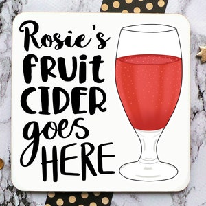 May include: White coaster with black text that reads "Rosie's fruit cider goes here" and a red glass of fruit cider.
