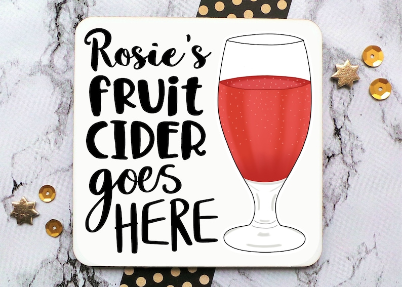 May include: White coaster with black text that reads "Rosie's fruit cider goes here" and a red glass of fruit cider.