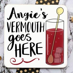 Puede incluir: Posavasos blanco con texto negro que dice "Angie's Vermouth goes HERE" con un remolino rojo debajo. A la derecha se muestra un vaso de l&iacute;quido rojo con cubitos de hielo y un agitador de madera.
