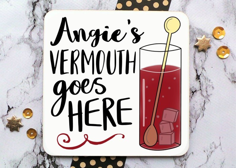 Puede incluir: Posavasos blanco con texto negro que dice "Angie's Vermouth goes HERE" con un remolino rojo debajo. A la derecha se muestra un vaso de l&iacute;quido rojo con cubitos de hielo y un agitador de madera.