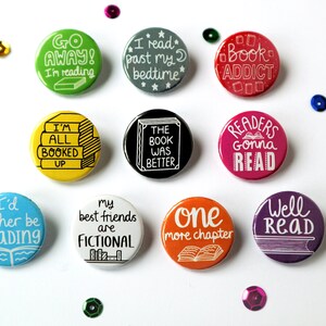 May include: Ten round button pins with various book-themed sayings. The buttons are colorful and feature white text. Some of the sayings include "I'd rather be reading", "Go Away! I'm reading", "I read past my bedtime", "Book Addict", "I'm all booked up", "The book was better", "Readers gonna read", "My best friends are fictional", "One more chapter", and "Well read".
