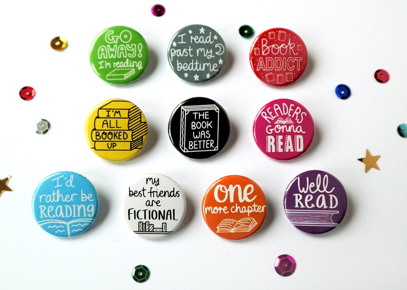 May include: Ten round button pins with various book-themed sayings. The buttons are colorful and feature white text. Some of the sayings include "I'd rather be reading", "Go Away! I'm reading", "I read past my bedtime", "Book Addict", "I'm all booked up", "The book was better", "Readers gonna read", "My best friends are fictional", "One more chapter", and "Well read".