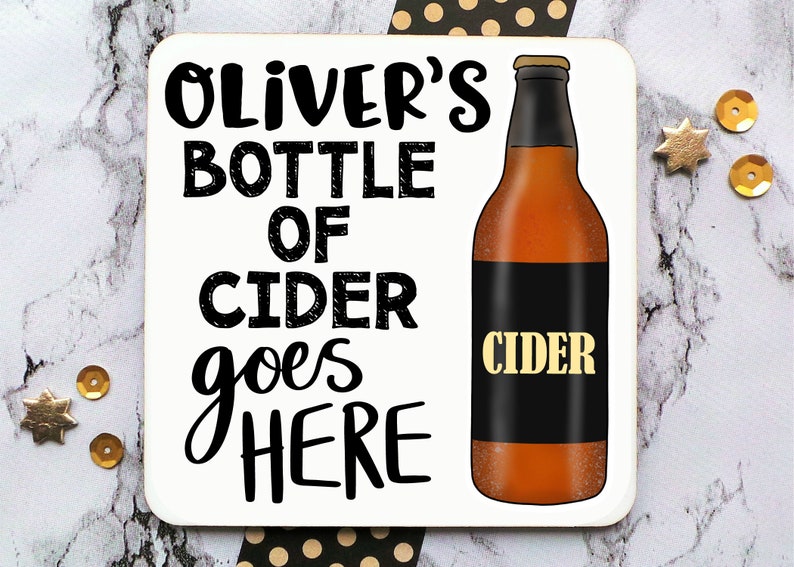 May include: A white coaster with black text that reads "Oliver's Bottle of Cider goes here". A brown bottle of cider with a black label that reads "Cider" is pictured on the right side of the coaster.