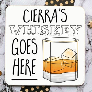 May include: White coaster with black text that reads "Cierra's Whiskey Goes Here" with a line underneath the text. A cartoon drawing of a glass of whiskey with ice cubes is to the right of the text.