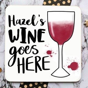 Puede incluir: Posavasos blanco con texto negro que dice "Hazel's Wine goes HERE" y una copa de vino tinto con salpicaduras de vino tinto.