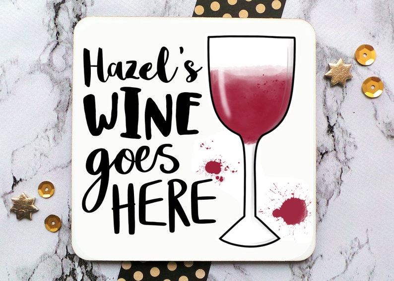 Puede incluir: Posavasos blanco con texto negro que dice "Hazel's Wine goes HERE" y una copa de vino tinto con salpicaduras de vino tinto.