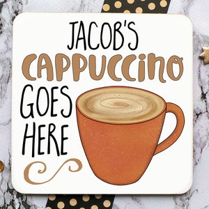 Op de afbeelding: Witte onderzetter met de tekst "Jacob's Cappuccino Goes Here" in zwarte en bruine letters. Op de onderzetter is een bruine koffiemok met een swirl van bruine koffie afgebeeld.