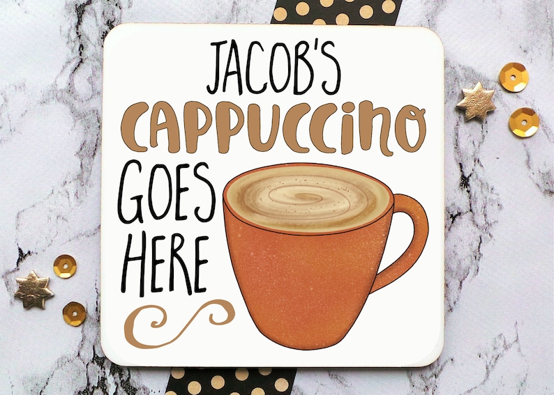 Op de afbeelding: Witte onderzetter met de tekst "Jacob's Cappuccino Goes Here" in zwarte en bruine letters. Op de onderzetter is een bruine koffiemok met een swirl van bruine koffie afgebeeld.