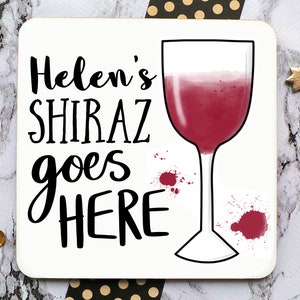 Puede incluir: Posavasos blanco con texto negro que dice "Helen's Shiraz goes HERE" y un dibujo de contorno negro de una copa de vino con vino tinto dentro. Hay salpicaduras de vino tinto en el posavasos.