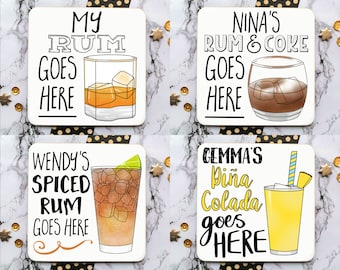 May include: Four white square coasters with black text and illustrations of cocktails. The coasters feature the text "My Rum Goes Here", "Wendy's Spiced Rum Goes Here", "Nina's Rum & Coke Goes Here", and "Gemma's Piña Colada Goes Here".