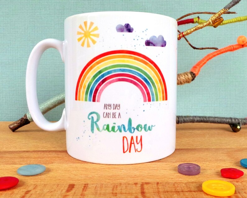 Puede incluir: Taza de cer&aacute;mica blanca con un dise&ntilde;o de arco&iacute;ris y el texto "Any day can be a rainbow day".