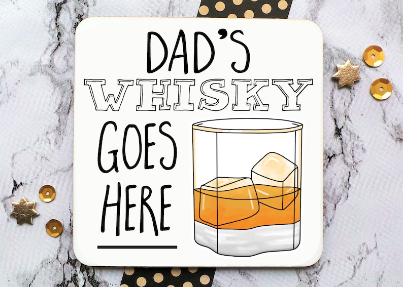 May include: White coaster with black text that reads "Dad's Whisky Goes Here" with a line underneath the text. A black line drawing of a glass of whiskey with ice cubes is to the right of the text.