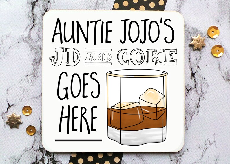 May include: A white coaster with black text that reads "Auntie Jojo's JD and Coke goes here" with a line underneath the text. A cartoon drawing of a glass of brown liquid with ice cubes is to the right of the text.
