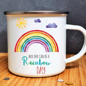 Puede incluir: Taza de esmalte blanco con un dise&ntilde;o de arco&iacute;ris, sol y nubes. El texto dice "Any day can be a Rainbow Day".