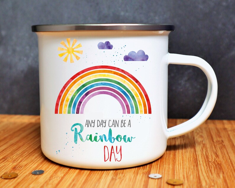 Puede incluir: Taza de esmalte blanco con un dise&ntilde;o de arco&iacute;ris, sol y nubes. El texto dice "Any day can be a Rainbow Day".