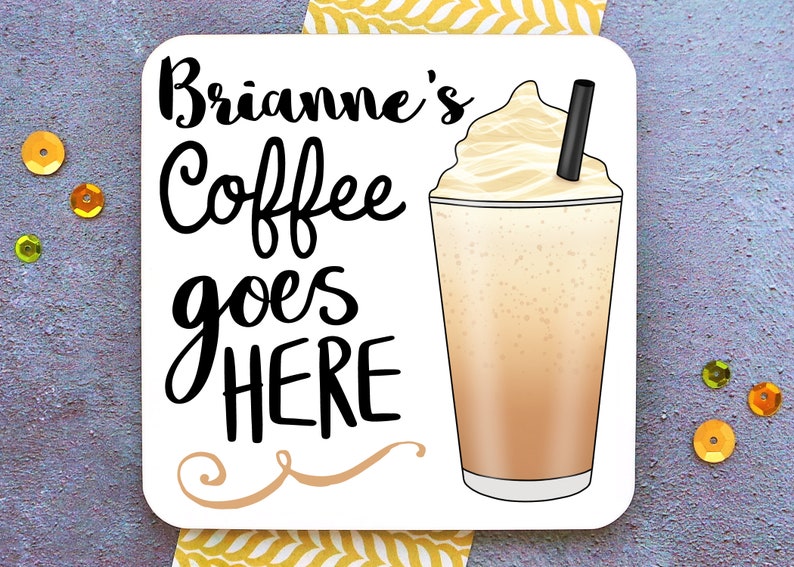 Op de afbeelding: Witte vierkante onderzetter met zwarte tekst die "Brianne's Coffee goes HERE" luidt, met een decoratieve krul eronder. Aan de rechterkant van de onderzetter staat een cartoonafbeelding van een ijskoffie met slagroom en een rietje.