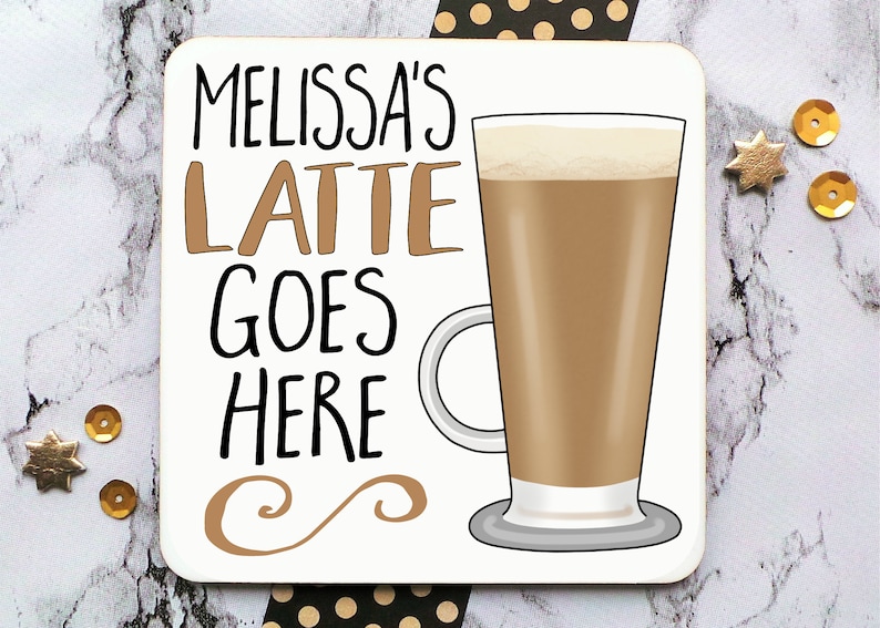 Op de afbeelding: Witte onderzetter met zwarte tekst die "Melissa's Latte Goes Here" luidt en een bruine illustratie van een latte in een glas. De onderzetter heeft een bruin swirl-ontwerp in de rechterbenedenhoek.