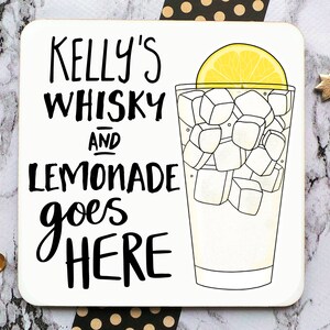 May include: A white coaster with black text that reads "Kelly's Whisky and Lemonade goes HERE". A black and white illustration of a glass of lemonade with a lemon wedge on top is on the right side of the coaster.