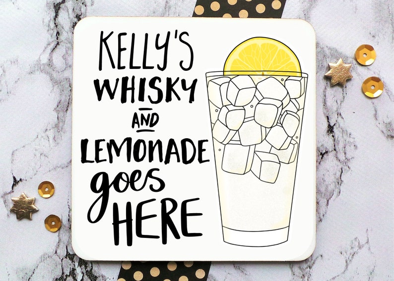 May include: A white coaster with black text that reads "Kelly's Whisky and Lemonade goes HERE". A black and white illustration of a glass of lemonade with a lemon wedge on top is on the right side of the coaster.